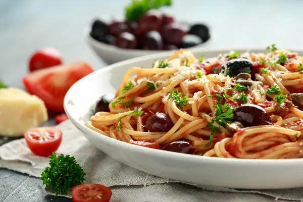 Un piatto invitante di pasta alla puttanesca, con spaghetti conditi con pomodoro, olive nere e prezzemolo fresco.