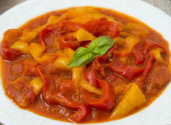 Peperonata ricetta della nonna: peperoni rossi e gialli stufati in un sugo saporito, guarniti con una fogliolina di basilico.