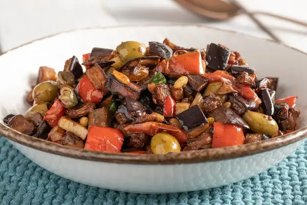 Un invitante piatto di caponata di verdure, con melanzane, peperoni rossi, olive verdi e capperi, pronto per essere gustato.