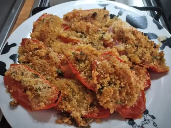Pomodori al forno ripieni di pangrattato e erbe aromatiche, dorati e invitanti.