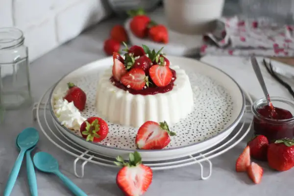 Deliziosa panna cotta con fragole fresche e salsa di fragole, guarnita con panna montata e foglioline di menta.