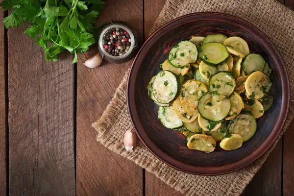 Piatto di zucchine trifolate, condite con aglio, prezzemolo e pepe, su un tavolo di legno rustico.