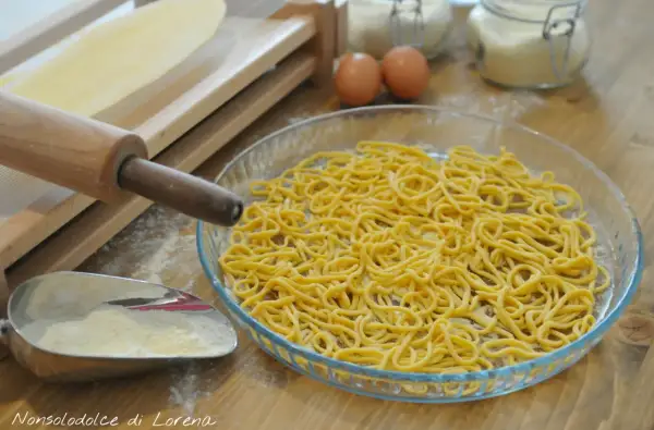 Spaghetti alla chitarra appena fatti, pronti per essere cucinati. Ingredienti freschi e attrezzi per la pasta sul tavolo.