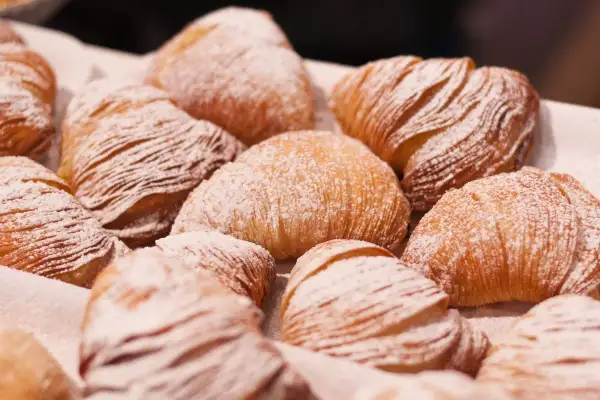 Un gruppo di sfogliatella riccia, dolci napoletani con pasta sfoglia croccante e ripieno cremoso, cosparsi di zucchero a velo.