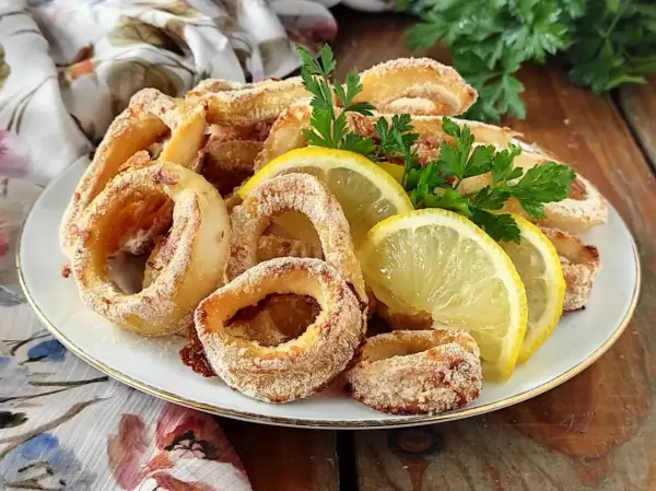 Anelli di calamari gratinati al forno, dorati e croccanti, guarniti con spicchi di limone e prezzemolo fresco.