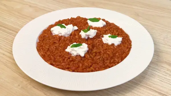 Un cremoso risotto al pomodoro, arricchito da ciuffi di ricotta fresca e basilico, servito su un piatto bianco.