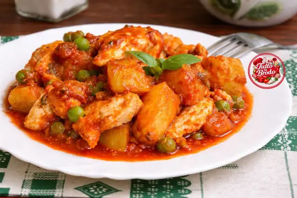 Un saporito spezzatino di pollo con patate e piselli in salsa rossa, guarnito con basilico fresco.