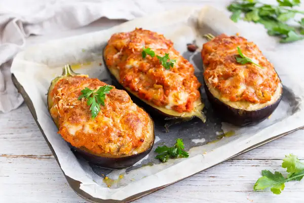 Melanzane ripiene al forno velocissime, dorate e filanti, guarnite con prezzemolo fresco su una teglia.