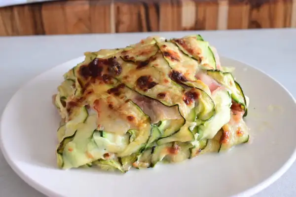 Una fetta di parmigiana di zucchine light, con strati di zucchine sottili, formaggio filante e prosciutto cotto, gratinata al forno.