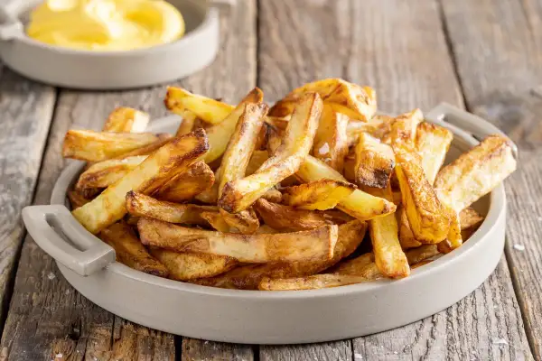Patate in friggitrice ad aria, dorate e croccanti, servite in una ciotola su un tavolo di legno.