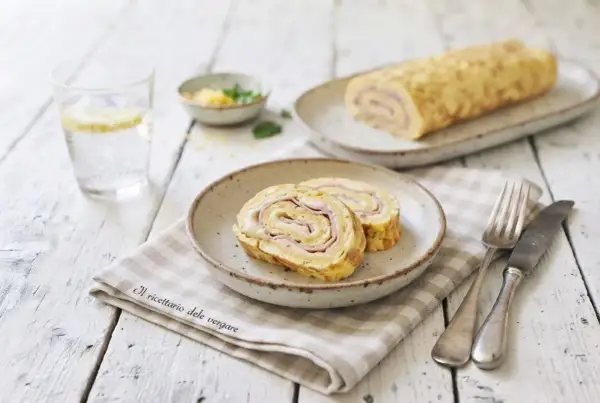 Delizioso rotolo di frittata con prosciutto e formaggio, servito su un piatto con una forchetta e un coltello.