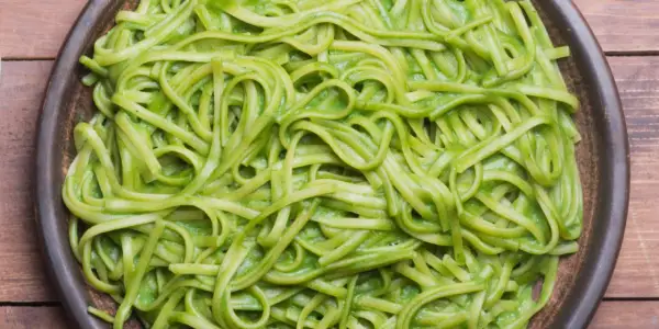 Pasta fresca condita con una cremosa salsa verde, probabilmente crema di zucchine per pasta, servita in un piatto scuro.