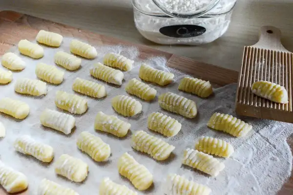 Gnocchi di patate ricetta: tanti piccoli gnocchi fatti in casa, pronti per essere cotti. Sullo sfondo, farina e un attrezzo per rigarli.