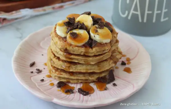 Pancake light con banana, cioccolato e sciroppo d'acero su un piatto rosa.