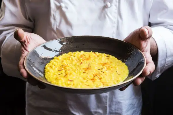 Chef presenta un cremoso risotto alla milanese, dorato e profumato, guarnito con fili di zafferano.